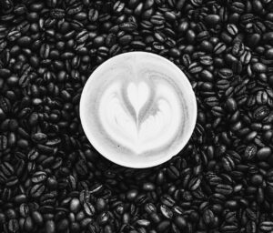 Black and white photo of a latte with heart-shaped latte art surrounded by coffee beans